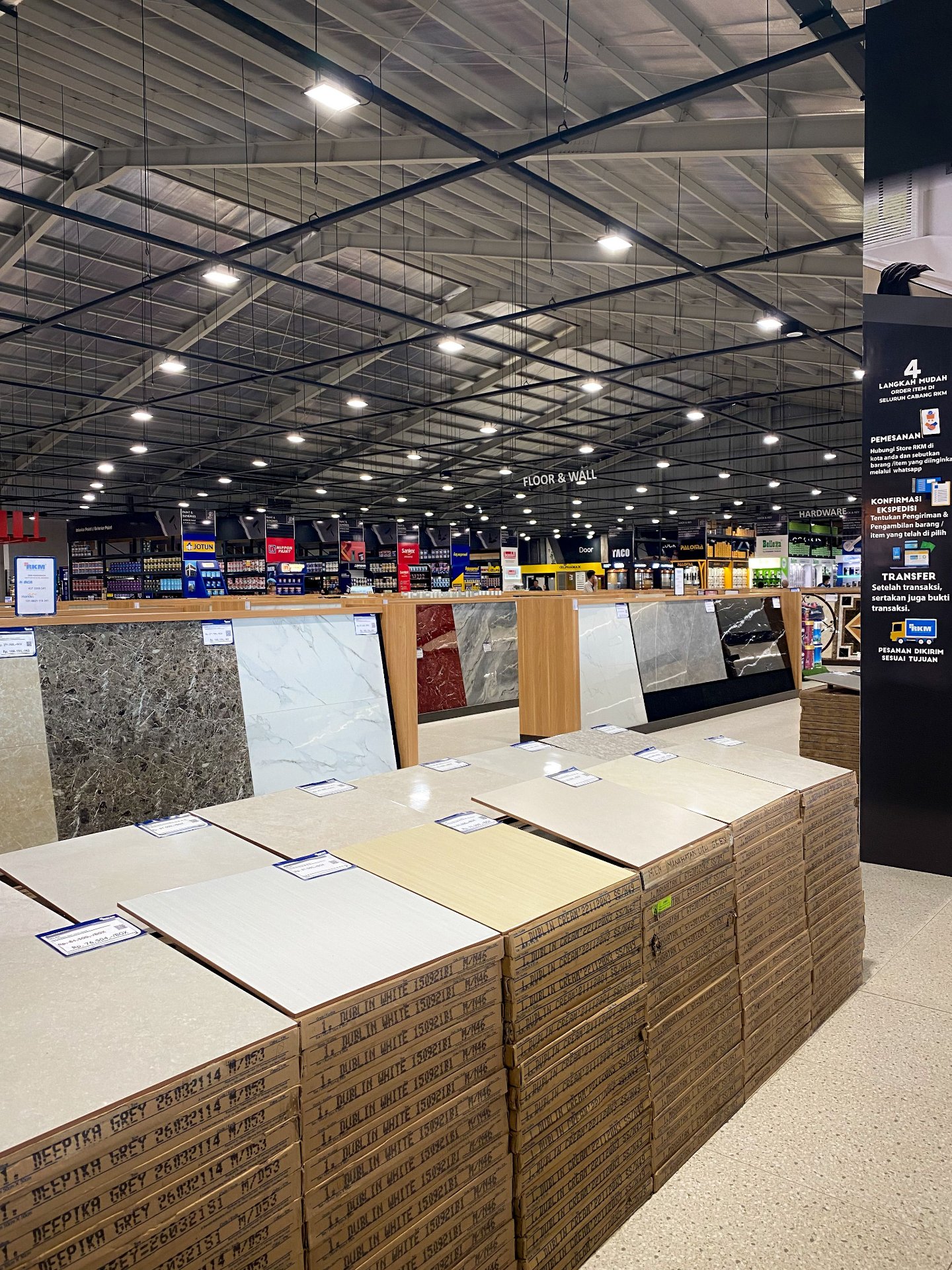 Azulejos tradicionais de cerâmica e porcelana expostos em prateleiras de um hipermercado de melhorias para o lar, mostrando acabamentos com aparência de pedra e mármore disponíveis para empreiteiros e proprietários